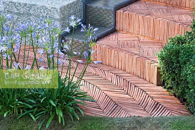 Agapanthus 'Blue Cloud' next to a herringbone tiled path and steps and a rainbow effect water feature. 'The Garden Lounge' - Silver Gilt Medal Winner - RHS Hampton Court Flower Show 2010 
 