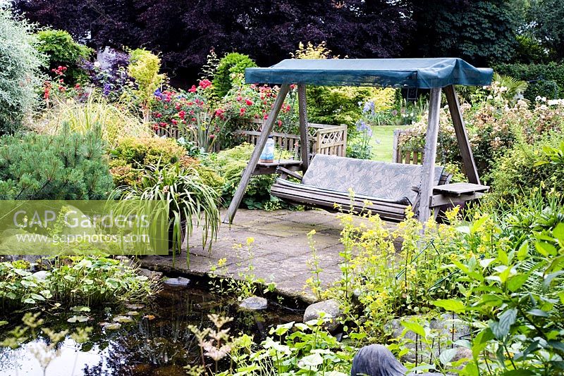Swinging seat by pond, perennials, mature trees and shrubs
