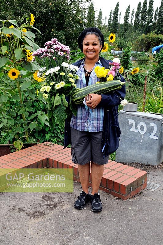 Smiling lady holding flowers and a marrow which she had just successfully bid for at an allotment show auction