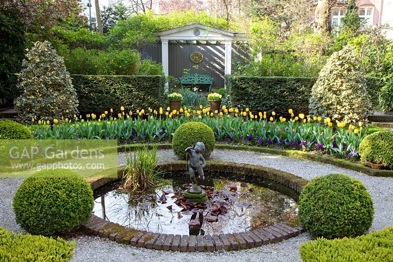 Formal garden with circular pond, beds of Tulipa 'Washington' and Tulipa 'Juliette' and clipped box balls 