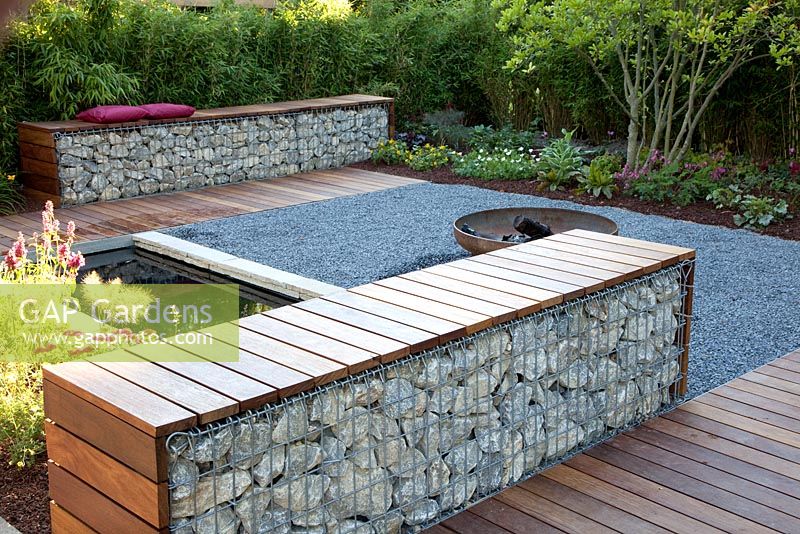 Small garden with patio, pond and benches made from wood and gabions backed by Fargesia murielae - Bamboo hedge