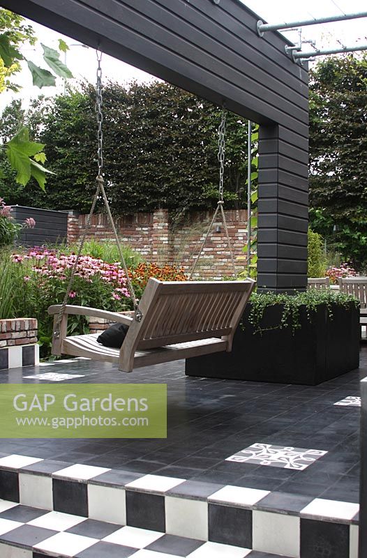 Wall as separation with hanging bench, black and white tiles on the terrace - Hobrede, Holland