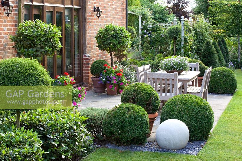 Patio with clipped Laurus nobilis standards and Ligustrum balls and wooden furniture