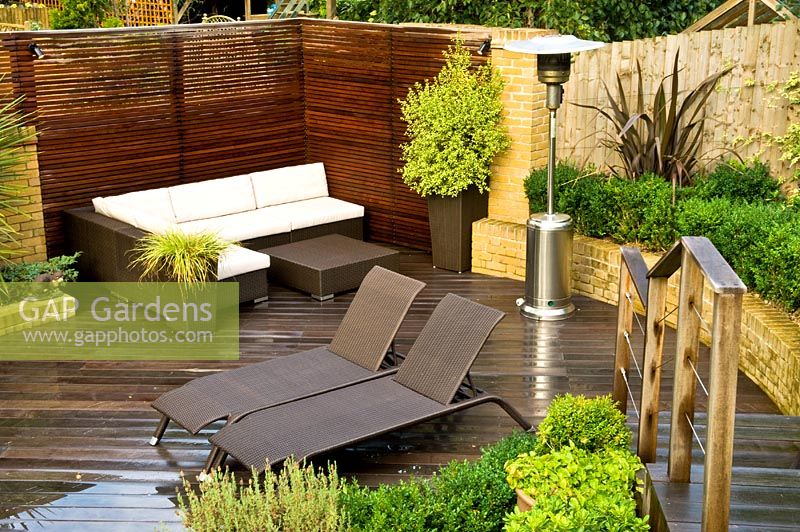 Small urban garden in September with contemporary furniture and patio heater on decking. Raised bed and planting of Lavandula - Lavender and Phormium. Muswell Hill, London