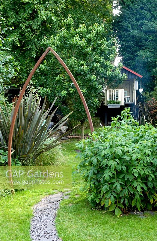 Urban garden with metal arch over slate path. Border with Phormium -New Zealand Flax. Yulia Badian, London, UK
 