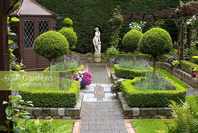 Secluded parterre garden with paths and walls made from reclaimed cobbles, station platform tiles and bricks, parterre with Buxus sempervirens - Box hedges, Lavandula angustifolia 'Hidcote' and Thuja topiary standards, pergola, summer house and classical garden statue - Brocklebank Road, Southport, Lancashire NGS 
