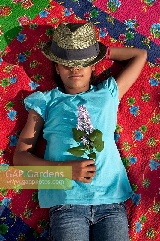 Girl asleep on blanket in the garden whilst holding purple flower
