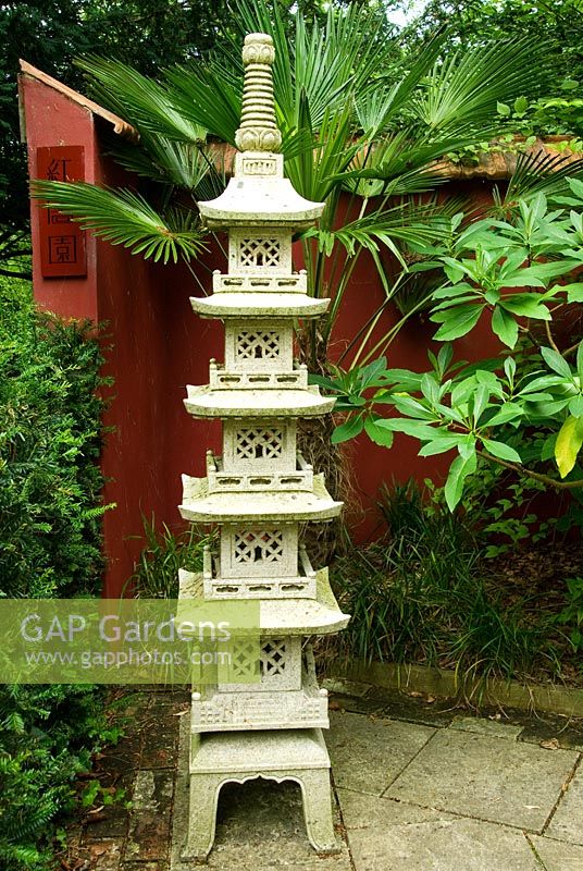 Chinese granite pagoda in the Red Wall garden planted around with palm Trachycarpus wagnerianus and Edgeworthia chrysantha. Beggars Knoll, Newtown, Westbury, Wiltshire, UK