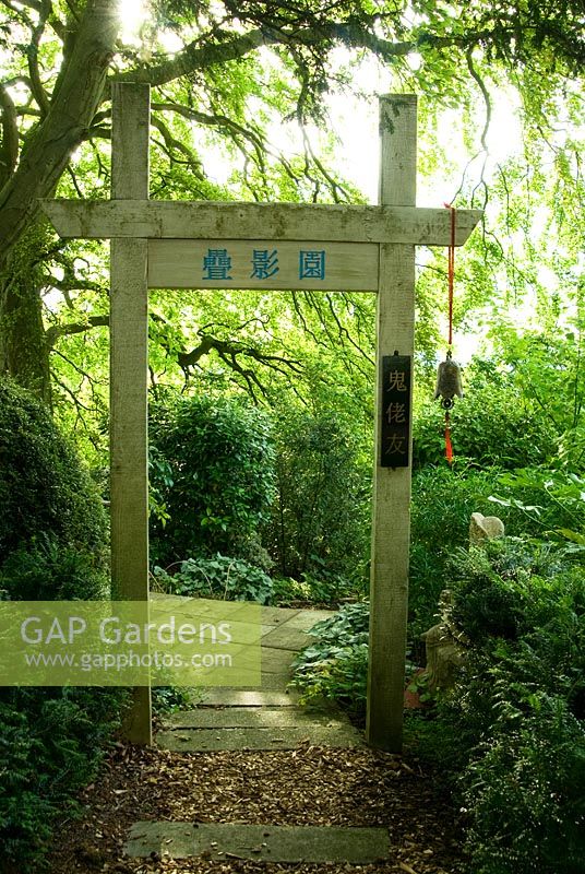 Chinese gateway marking entrance to garden of 10,000 Shadows planted with mostly non-Chinese plants, hence the vertical sign 'Friendship with foreign devils'. Chinese buddha on right. Beggars Knoll, Newtown, Westbury, Wiltshire, UK