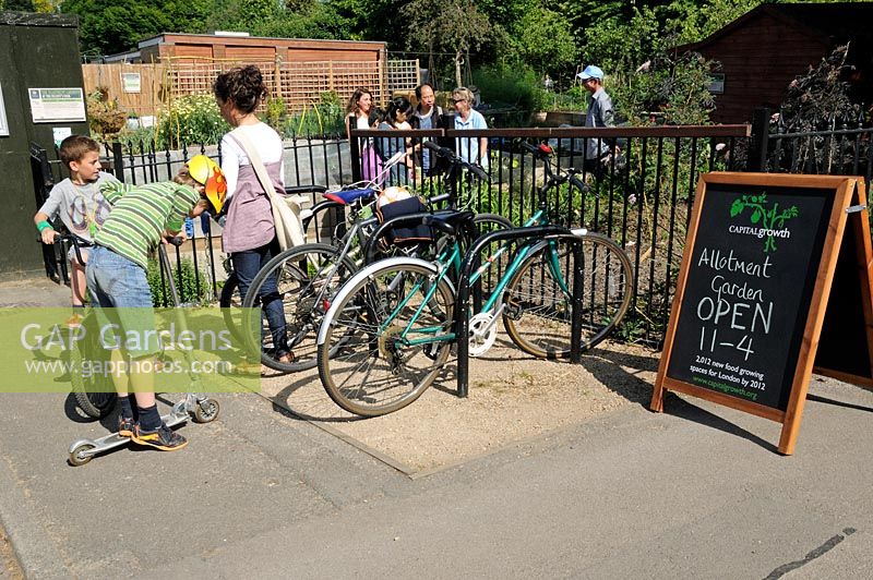 People attending a Capital Growth allotment garden open day with children, bikes and a billboard advertising the event in the forground. The Regent's Park Allotment Garden, Central London.
