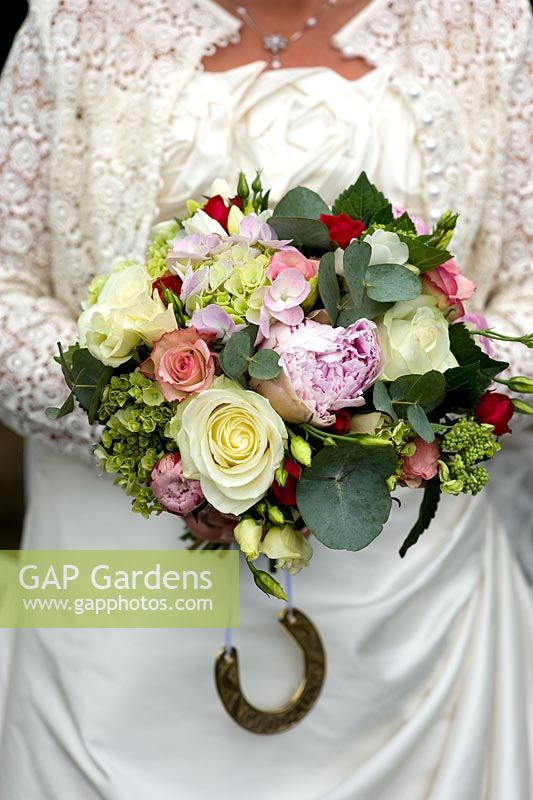 Woman in a wedding dress holding a brides bouquet of roses and peony