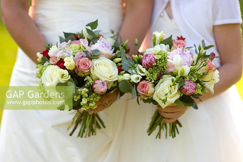 Woman and girl in a wedding dress holding brides and bridesmaids bouquet of roses and peony