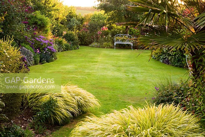 Lawn framed with Hakonechloa macra 'Aureola'. Poppy Cottage Garden, Roseland Peninsula, Cornwall, UK