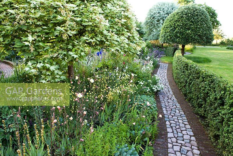 The Corner House, Wiltshire. Summer garden, cobble and brick paths wind their way through informal borders