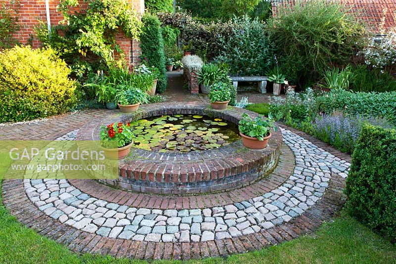 The Corner House, Wiltshire. Summer garden, small brick circular pond with lily pads