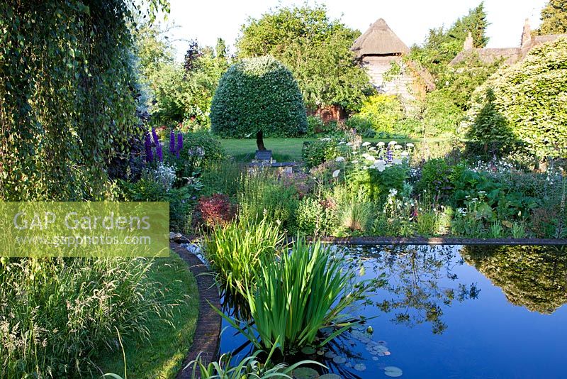 The Corner House, Wiltshire. Summer garden, large formal pond surrounded by informal planting