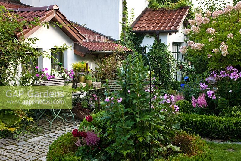 Wooden iron garden furniture decorated with containers next to box edged plantings with, Astilben, Buxus, Hydrangea paniculata and Phlox paniculata