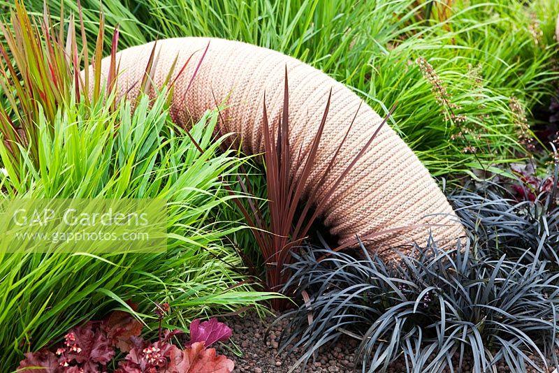 RHS Gardeners World Live 2011. The Birmingham Borders. 'Honey I shrank the Shed', designed by Simon Webster. Silver Gilt Medal. Giant worm made of coiled rope. Heuchera 'Mahogany', Heuchera 'Chocolate Ruffles', Hakonechloa macra, Panicum virgatum 'Rehbraun', Panicum virgatum 'Northwind', Miscanthus sinensis 'Herman Mussel', Imperata cylindrica 'Rubra', Ophiopogon planiscapus 'Nigrescens', Cordyline australis 'Red Star'