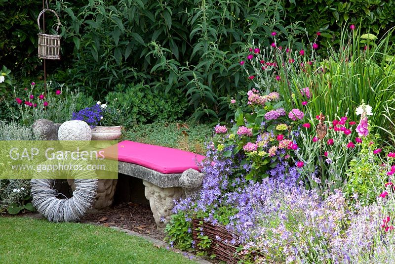 Stone bench with willow decorations next to border of  Hydrangea, Campanula poscharskyana and Lavandula - Lavender - Scheper Town Garden 