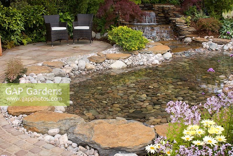Waterfall and pebble and cobble edged pool adjacent to patio and seats. Aughton Green Landscapes 'The Water Garden' designed by Harry and Astrid Levy. RHS Tatton Flower Show 2011