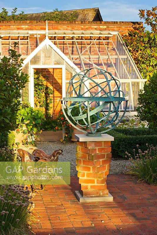 Metal armillary sundial and hen statue on red brick patio, Oxfordshire