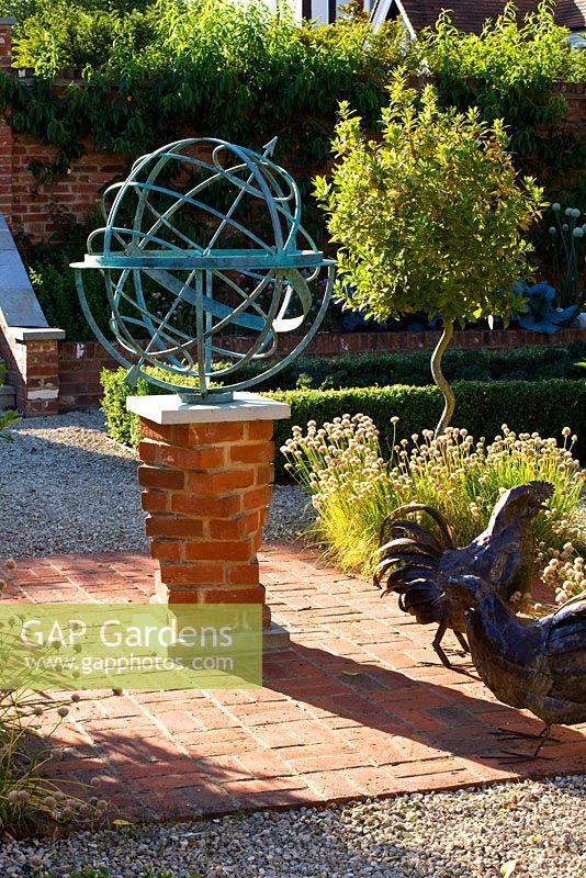 Metal armillary sundial and hen statue on red brick patio, Oxfordshire
