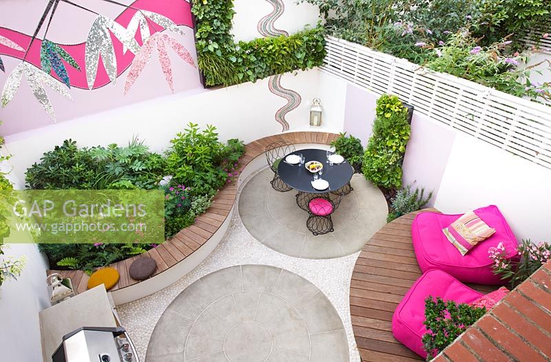 Elevated view of small patio garden with decking, pink chairs, mosaic by Celia Gregory, London.
