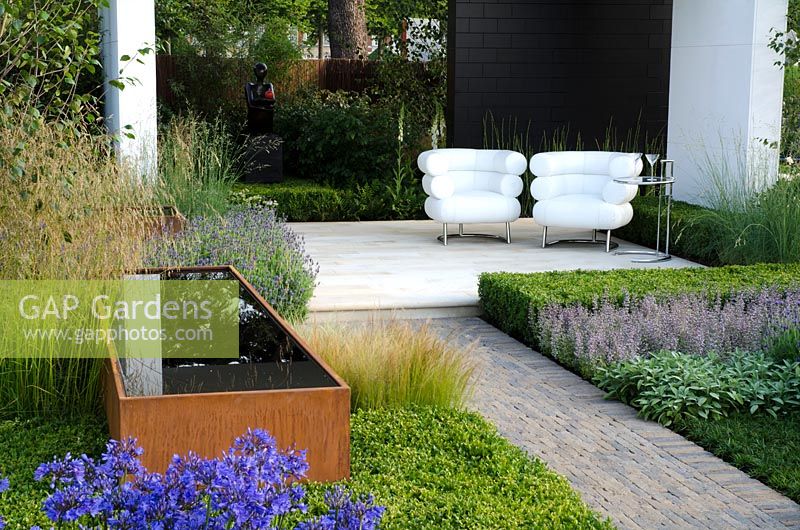 Cor-Ten steel water trough surrounded by Agapanthus, Stipa tenuissima and Lavandula, next to a black and white pavilion with white chairs - Vestra Wealth's Gray's Garden', Gold Medal Winner, RHS Hampton Court Flower Show 2011
