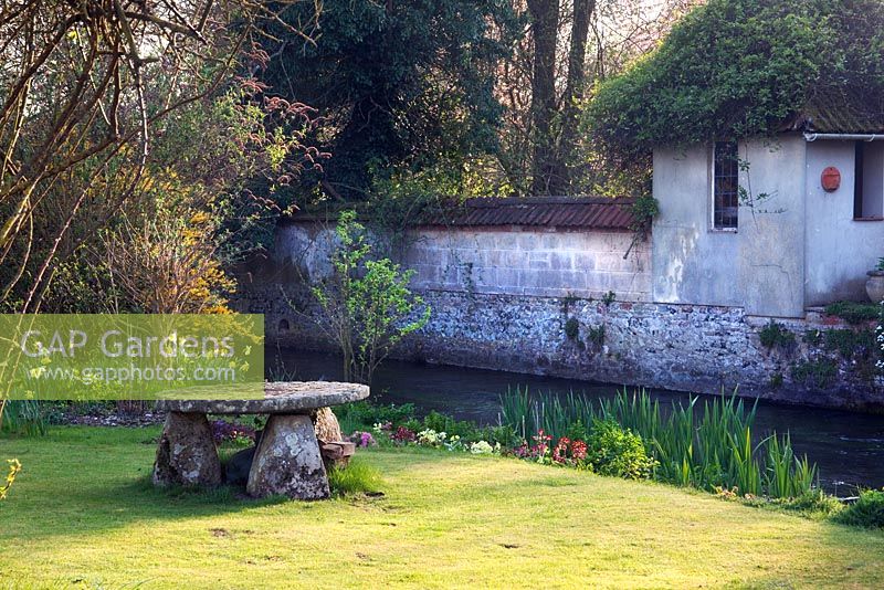 Old millstone used as table on lawn overlooking the River Till - Mill House, Wylye Valley, Wiltshire