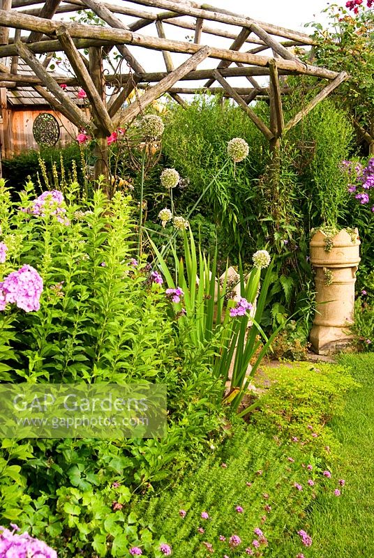 Wooden pergola surrounded by phlox, flowering leeks and Phuopsis stylosa