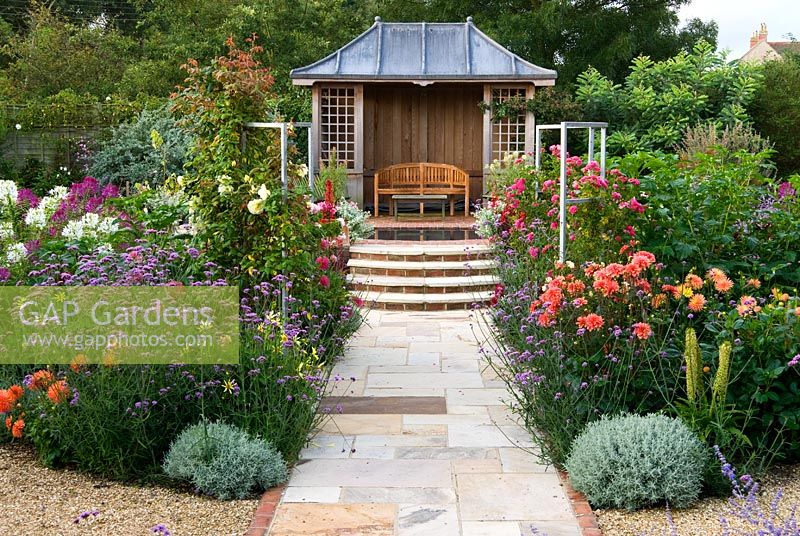 Central pond and summerhouse feature in the sunken garden, constructed in 2005, surrounded by a colourful mass of perennials and annuals including Eucomis, Verbena bonariensis, Dahlias, Roses, Cleomes and scarlet Lobelia cardinalis - Isle of Wight, UK
