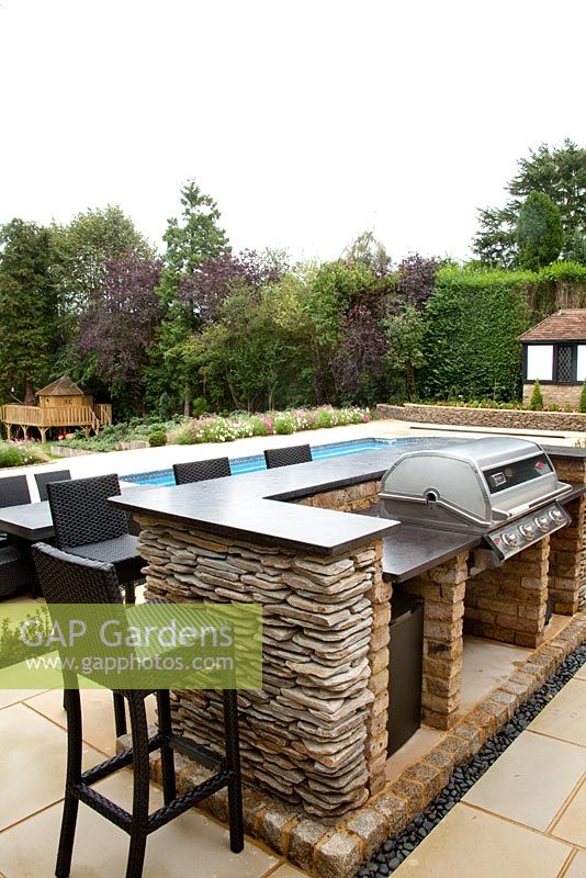 Suburban modern garden in early autumn with breakfast bar, swimming pool and barbecue on sandstone patio 
