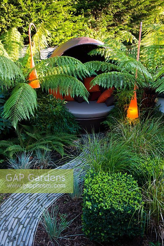 Contemporary light and covered seating area surrounded by Dicksonia antarctica and Polystichum setiferum ferns 