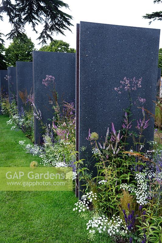 Herbaceous perennial planting between repeating vertical panels of recycled plastic with granite-like effect