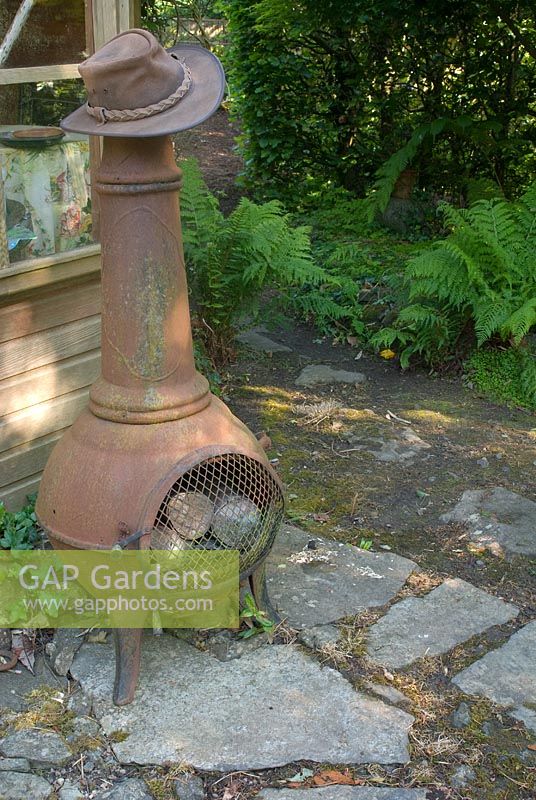 Chiminea by shed and stone path in shaded part of garden