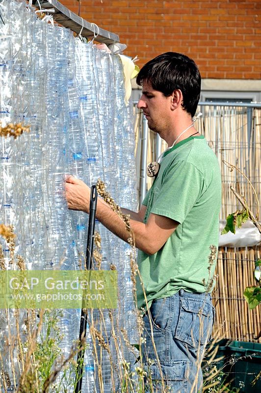 Man threading together recycled plastic bottles on the side of greenhouse. FOOD from the SKY a permaculture food growing and educational initiative on the roof top of Thornton's Budgens supermarket, Crouch End, Haringey, North London, UK
