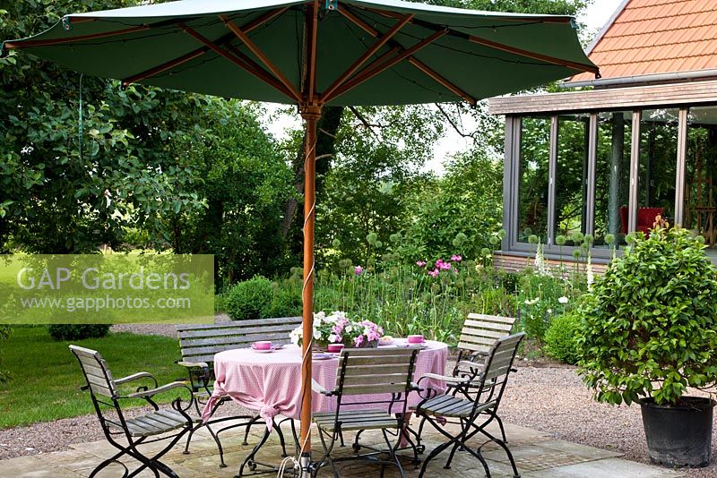 Relaxing area with wood and metal garden furniture and parasol. Planting includes - Allium aflatunense 'Purple Sensation', Buxus, Camellia japonica and Digitalis purpurea 'Alba' - Jens Tippel