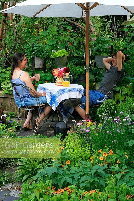 Small decorative kitchen garden planted with herbs, flowers, fruit and vegetables which includes a small table and chairs and suspended containers filled with salad vegetables