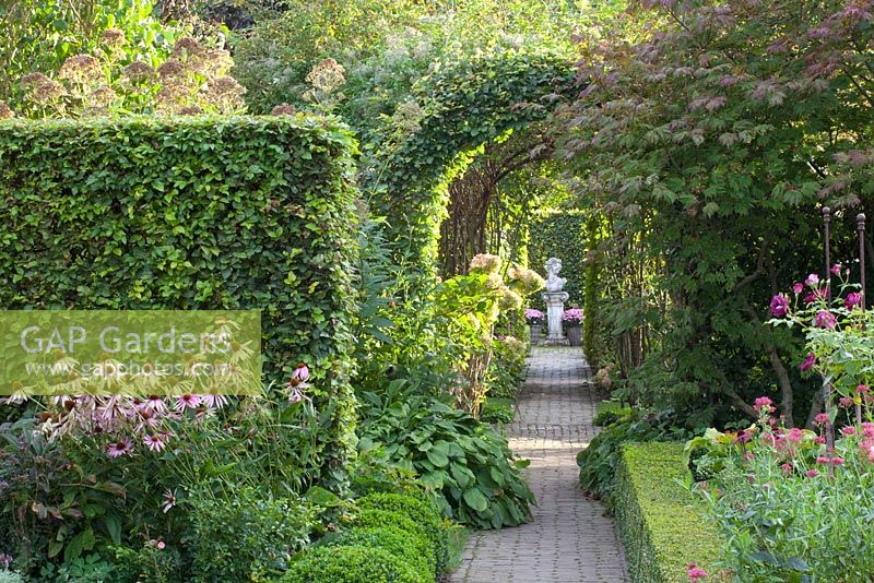 Path through formal garden with Fagus sylvatica - Beech hedging and statue focal point - Huys en Hof