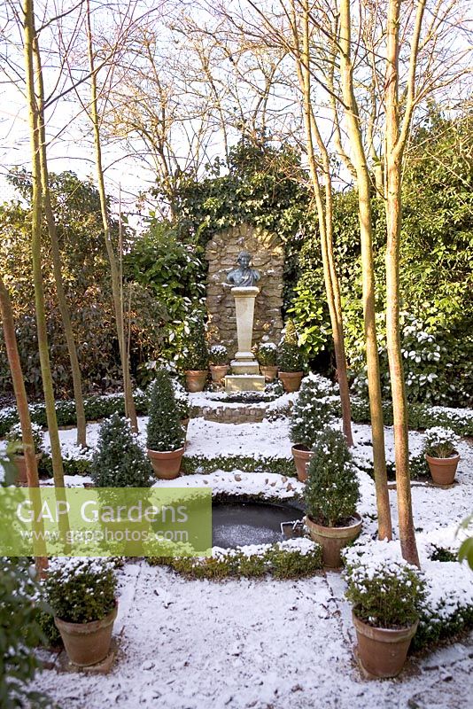 Formal garden with circular pond and evergreens in terracotta pots - The Old School House, Great Bentley, Essex in January
