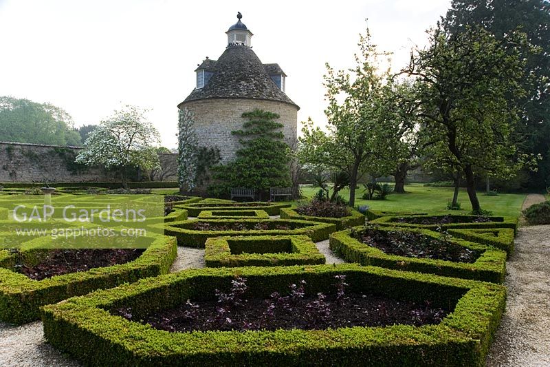 Pigeon House garden with pigeon house, 1685, box parterre, Cornus nuttallii and new red leaves of hybrid tea roses - Rousham House, Bicester, Oxon, UK