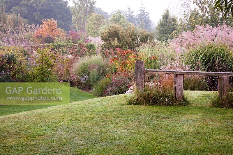 Landscaped hillock with decorative seat overlooking autumn borders - Marchants Hardy Plants Nursery, Sussex