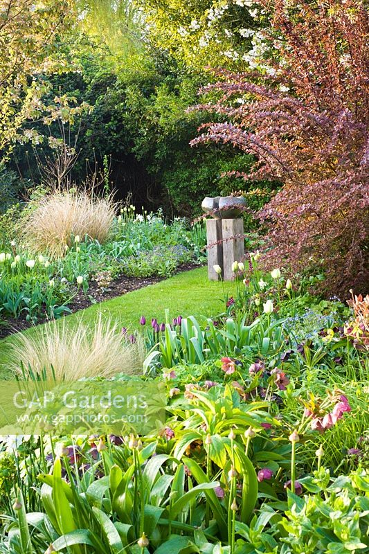 Modern sculpture and spring border with Tulipa 'Recreado' and 'Spring Green'. Other plants include Stipa, Hellebores and Narcissus 'Thalia'
