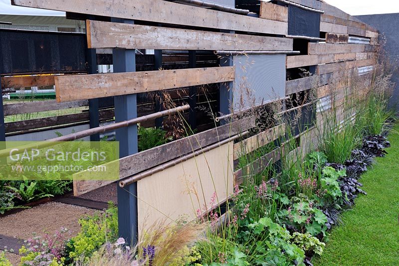 Grasses and perennials along fence constructed from reclaimed materials. 'Light At The End Of The Tunnel', Hampton Court Palace Flower Show 2012