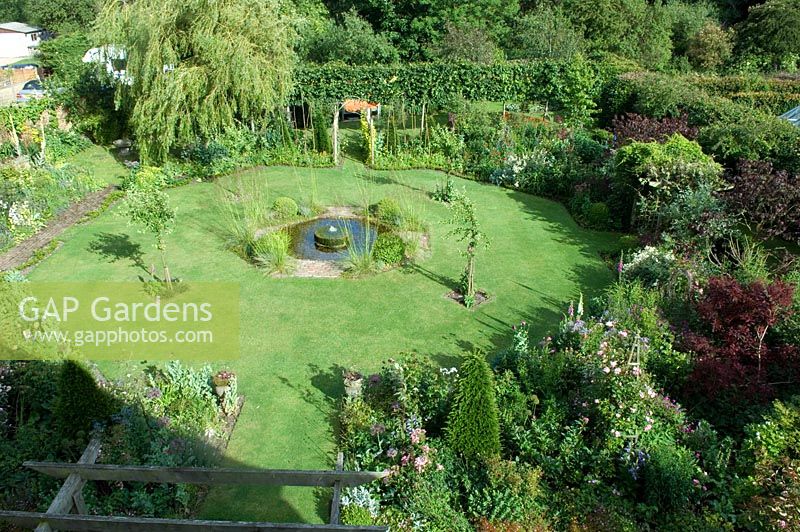 Overview of garden with hexagonal shaped lawn and central pond with millstone fountain