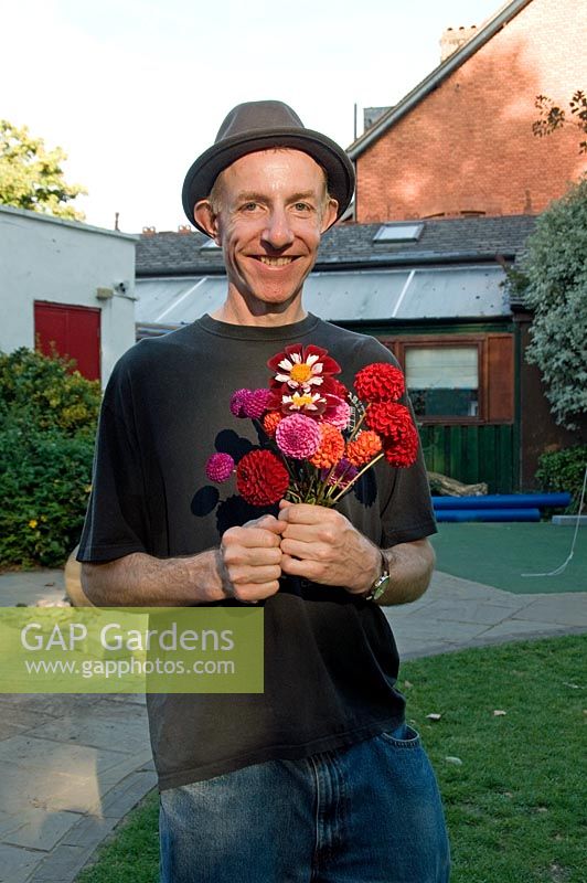 Man in pork pie type hat holding a bunch of mixed Dahlias 