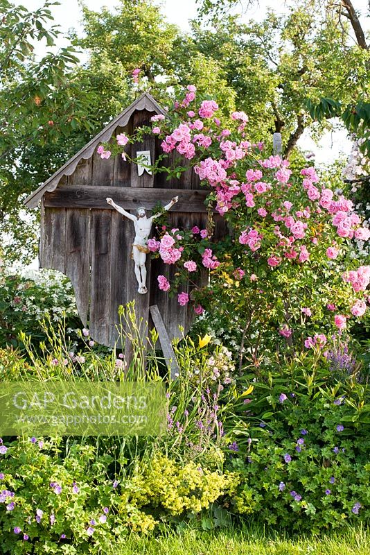 Bavarian wayside cross with climbing roses and perennials in a country garden