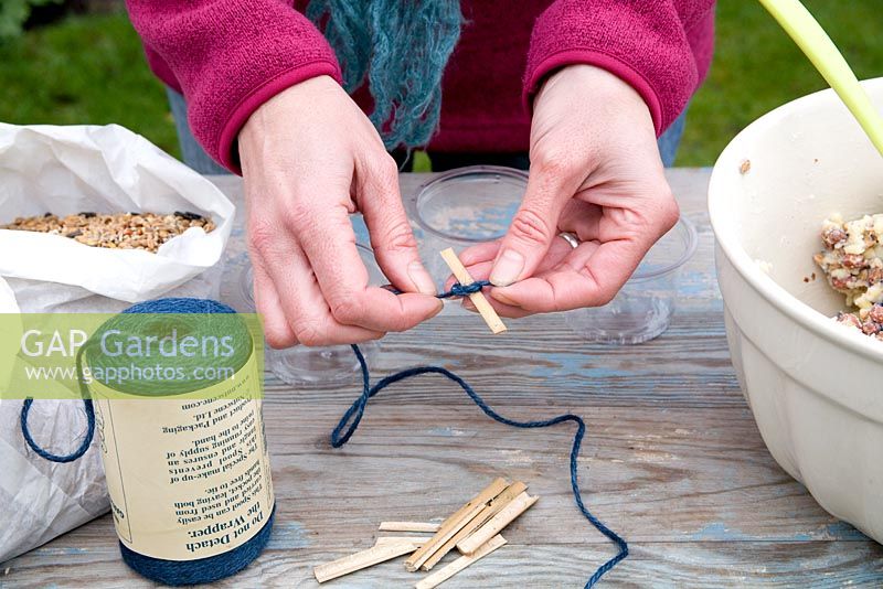 Step by step for creating hanging bird feeders out of teacups and yoghurt pots - tying thread to wooden sticks 