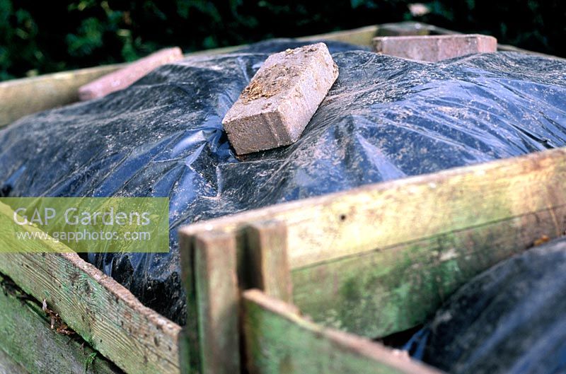 Wooden compost bins sealed with black polythene, weighted down with bricks, sealed to build up heat and quicken composting process and to hold moisture and prevent weeds from growing. 