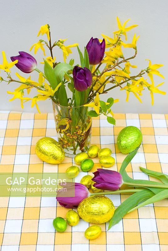 Flower arrangement of forsythia and purple tulips with foil wrapped easter eggs